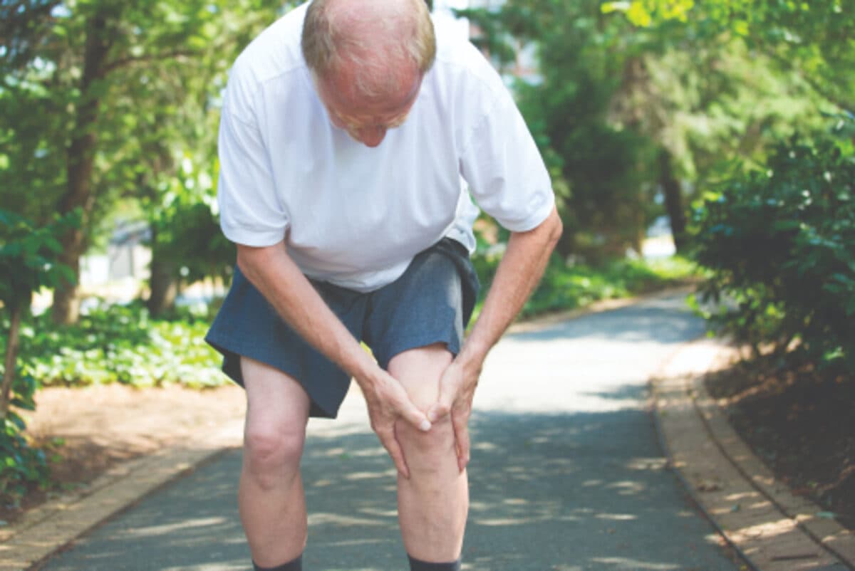 A man pausing to hold his knee on an outdoor walk